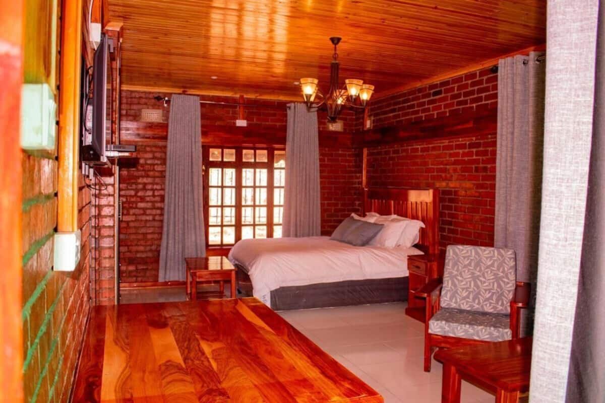 Um quarto com cama, cadeira, piso de madeira, parede de tijolos e um candelabro.