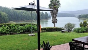 A patio with a view of a lake, a palm tree, and a grassy area with a bench. - Lake Alexander Country Resort  (Penhalonga)