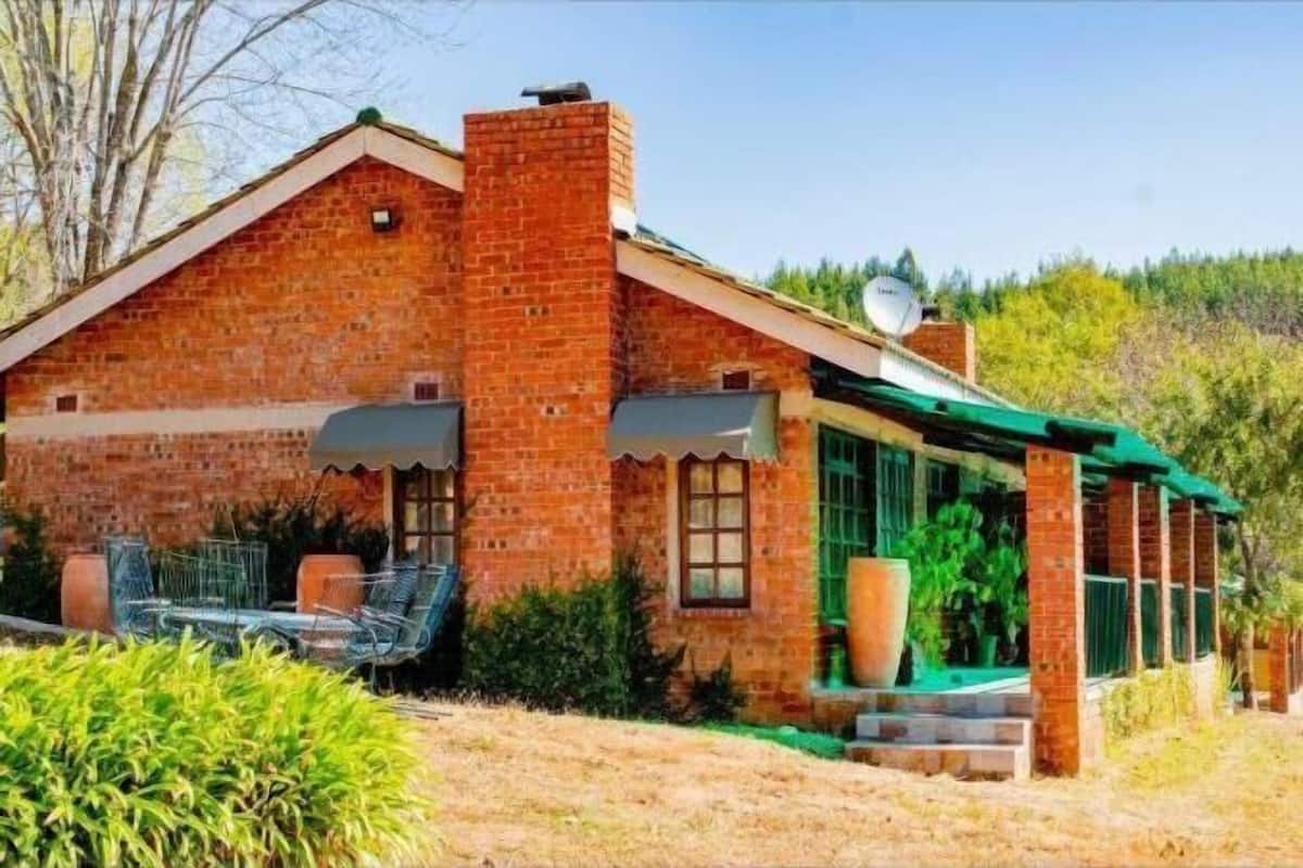 Uma casa de tijolos com telhado verde, antena parabólica e área de estar externa.