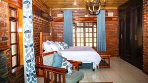 A room with a large bed, wooden furniture, a chandelier, and brick walls. - Lake Alexander Country Resort  (Penhalonga)