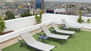 Une terrasse sur le toit, dotée de quatre chaises longues et d’une petite table, entourée de gazon synthétique, et offrant une vue sur un paysage urbain composé de différents bâtiments.