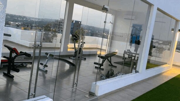 Une salle de sport moderne avec des murs en verre, divers appareils d’exercice et une vue sur le paysage urbain.
