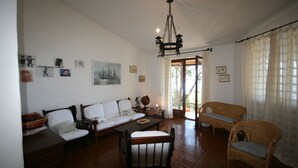 Uma sala de estar ampla com teto alto, lustre, sofá, mesa de jantar e móveis de vime.