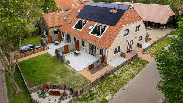 Una casa de dos pisos con techo inclinado, paneles solares, un patio con mobiliario exterior y un jardín vallado.