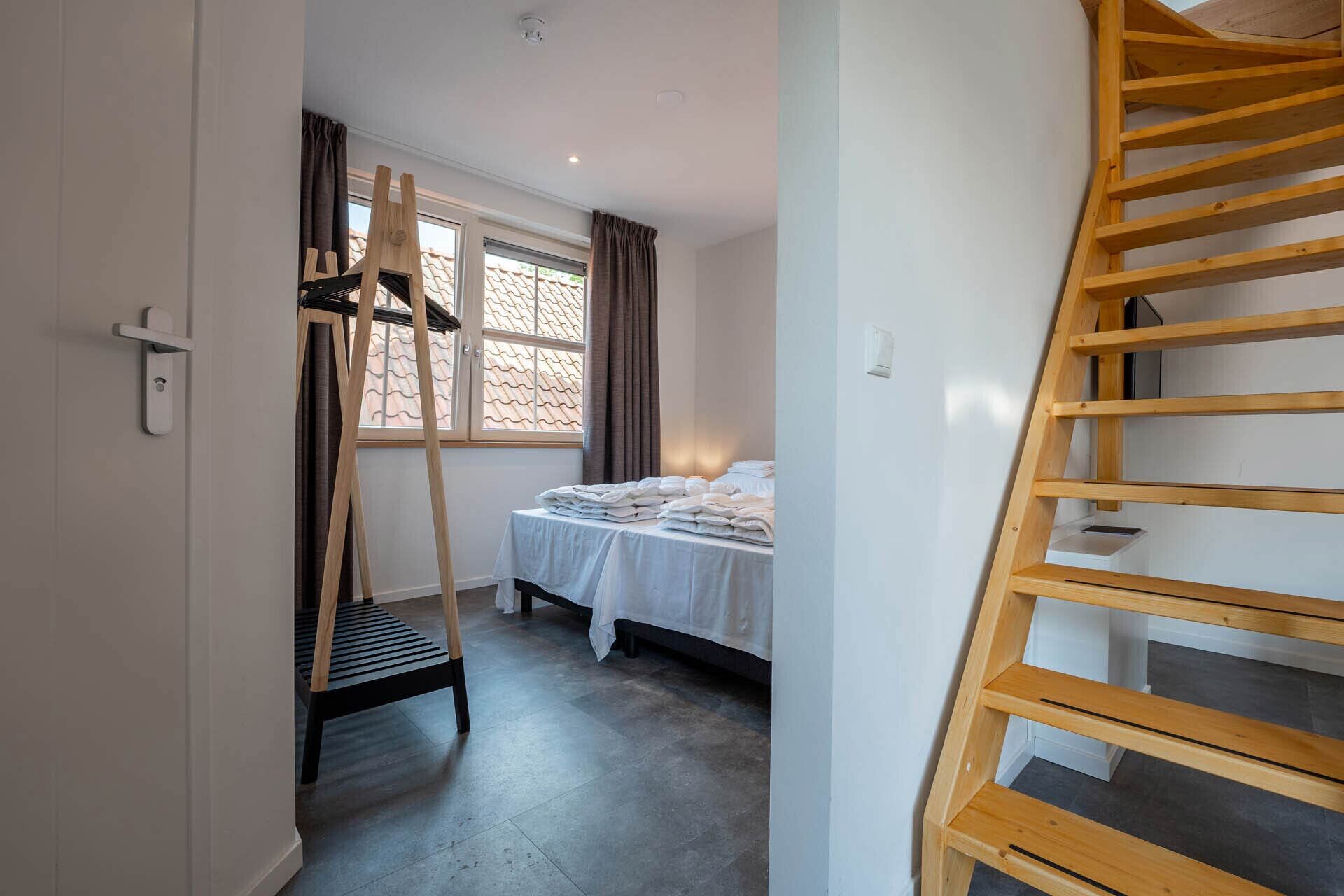 A bedroom with a bed, a wooden ladder, a window with curtains, and a door with a handle.