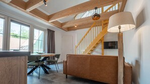 Ein modernes Interieur mit einer Holztreppe, einer Couch, einem Esstisch mit Stühlen und einem an der Wand befestigten Fernseher.