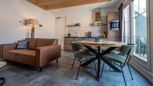 Ein modernes Wohnzimmer mit einem braunen Ledersofa, einem runden Holztisch mit Stühlen und einem großen Fenster mit Blick.