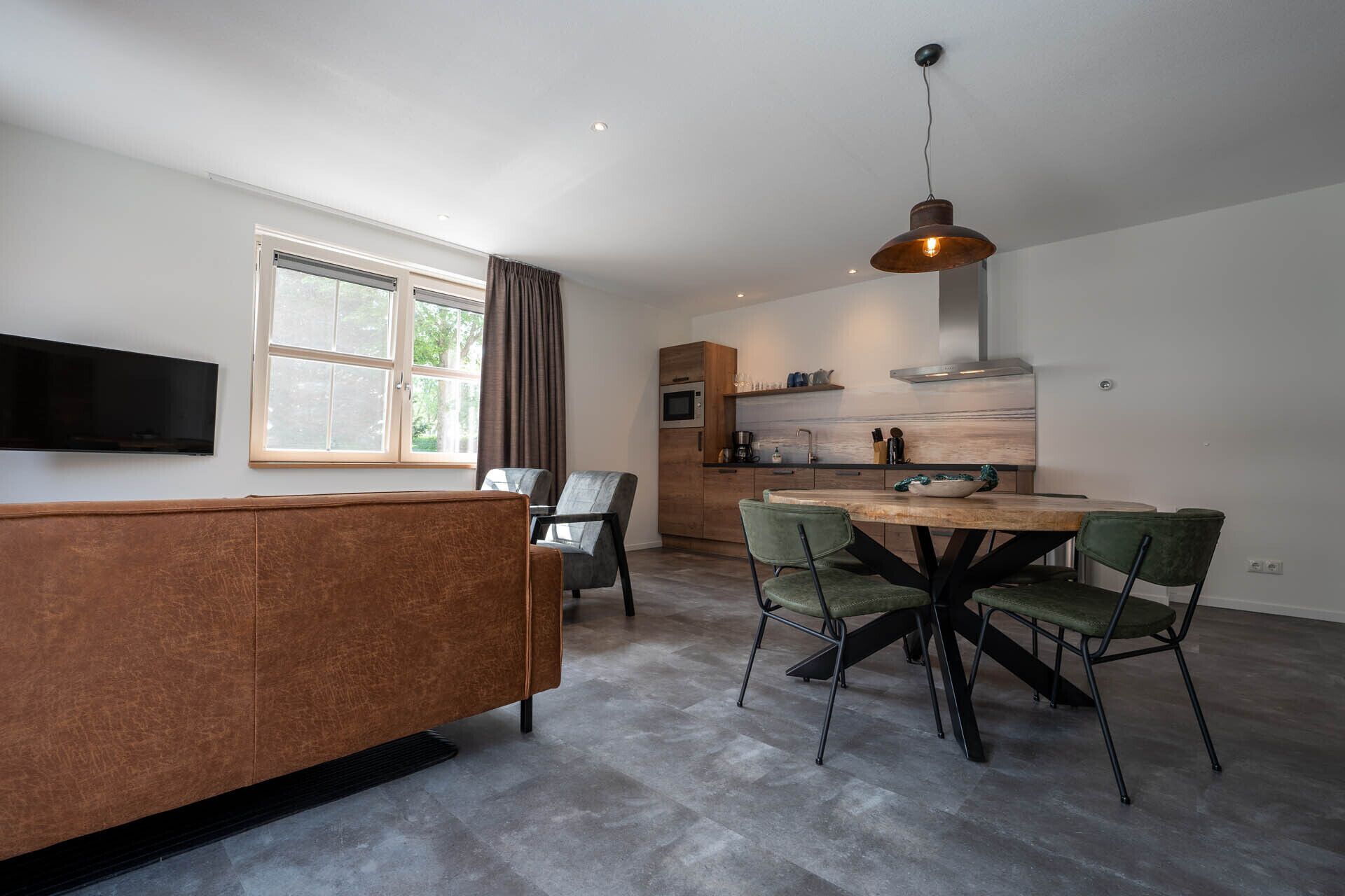 A modern kitchen with a dining area, featuring a wooden dining table, green upholstered chairs, and a built-in oven.