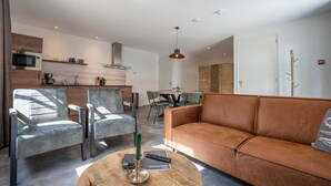 Een moderne woonkamer met een bruine bank, grijze fauteuils en een houten salontafel.