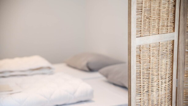 Een bed met witte beddengoed en een grijs kussen.
