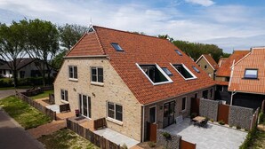 Een huis met twee verdiepingen, een schuin dak, een terras met buitenmeubels en een omheinde achtertuin.