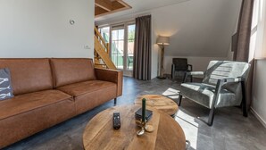 Ein modernes Wohnzimmer mit einem braunen Ledersofa, einem runden Holztisch, einem grauen Sessel und einer Stehlampe.