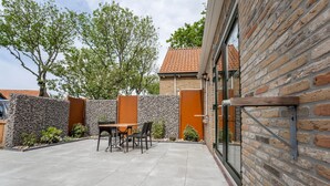 Eine Terrasse mit Tisch und Stühlen, eine Steinmauer und ein Backsteinhaus.