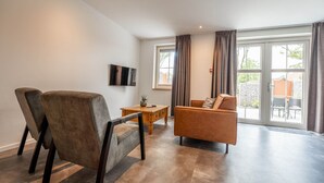 Ein modernes Wohnzimmer mit einer Couch, einem Sessel, einem Couchtisch und einem an der Wand befestigten Flachbildfernseher.