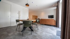 Ein modernes Wohnzimmer mit einem runden Holztisch, grünen Polsterstühlen, einem braunen Sofa und einem flachbildfernseher an der Wand.