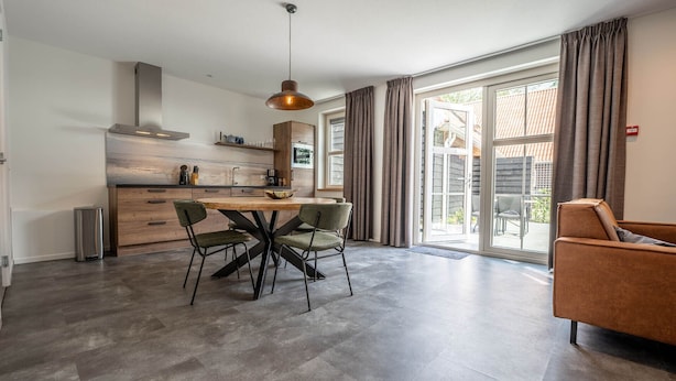 A modern kitchen with a dining area, large windows, and a sliding glass door leading to an outdoor patio. - De Witte Brugh- 't Fennoat (Buren)