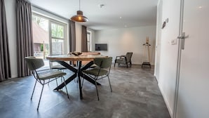 A modern dining area with a wooden table and four chairs, a pendant light, and a TV on the wall. - De Witte Brugh- 't Fennoat (Buren)