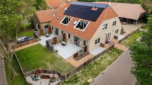 A two-story house with a sloped roof, solar panels, a patio with outdoor furniture, and a fenced garden area. - De Witte Brugh- 't Fennoat (Buren)