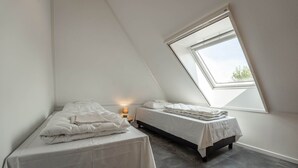 A small, well-lit attic bedroom with two beds, a skylight, and a bedside table with a lamp. - De Witte Brugh - Nijlânsrèèd (Buren)