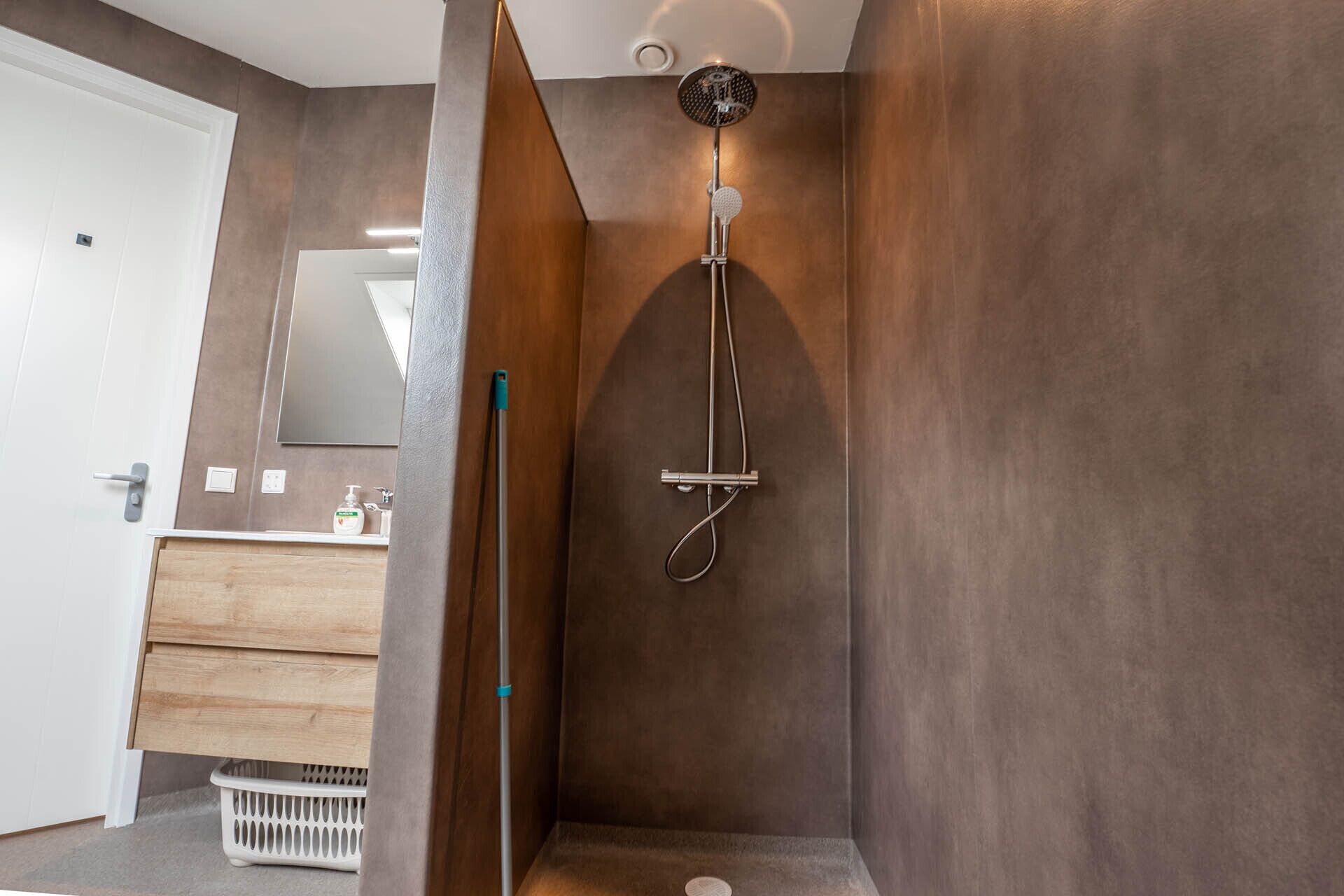 A modern bathroom with a shower, wooden vanity, and a mirror.