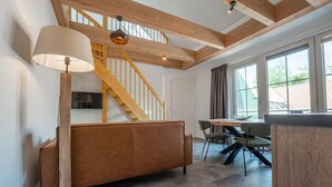 A modern interior with a wooden staircase, a sofa, a dining table with chairs, and a large window providing natural light. - De Witte Brugh - Nijlânsrèèd (Buren)