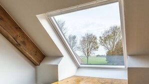 A room with a slanted ceiling and a skylight. A wooden table is positioned under the skylight, and a chair is placed beside it.