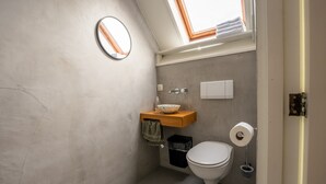 A compact bathroom with a skylight, a wooden vanity, a white toilet, and a trash bin.