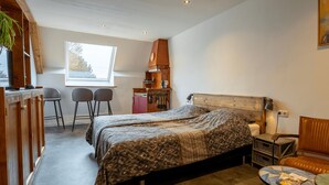 A bedroom with a bed, a desk, two chairs, a small table, a lamp, and a window.