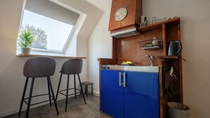 Een kleine keuken met een blauwe kast, een klok en een klein raam met een plant.