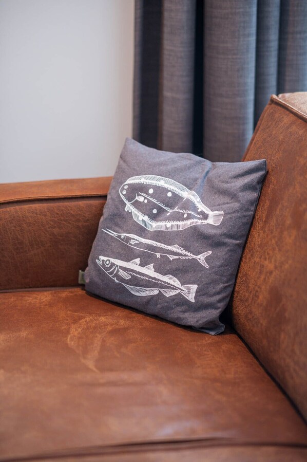 A grey pillow with fish designs on a brown leather sofa.