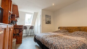 A bedroom with a bed, wooden wardrobe, kitchenette, and a window. - De Witte Brugh - Studio 4 (Buren)