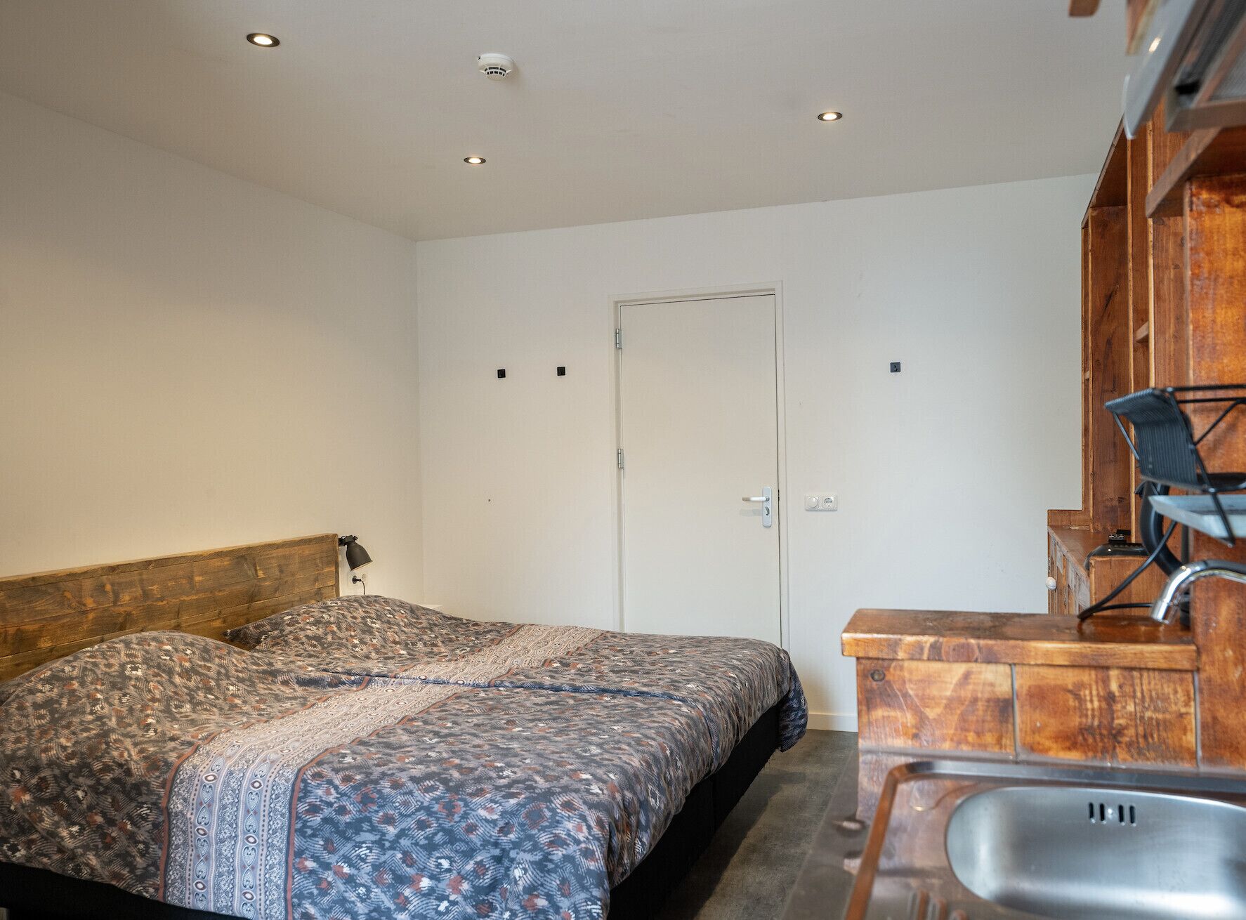 Un dormitorio con cama, cabecero de madera, escritorio con silla, puerta y una ventana pequeña.