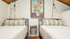 Una camera da letto con due letti, soffitto in legno, un quadro di girasoli e un piccolo tavolino.