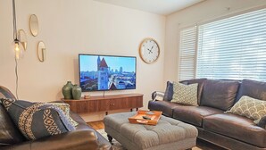 Un soggiorno con un'ampia televisione a schermo piatto, divani in pelle, un tavolino in legno e vista sulla città.