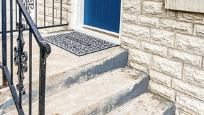 Facciata in pietra con una porta blu, un corrimano in metallo nero e un tappetino d'ingresso.