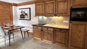 A kitchen with wooden cabinets, a black stove, and a dining table set with glasses and plates.