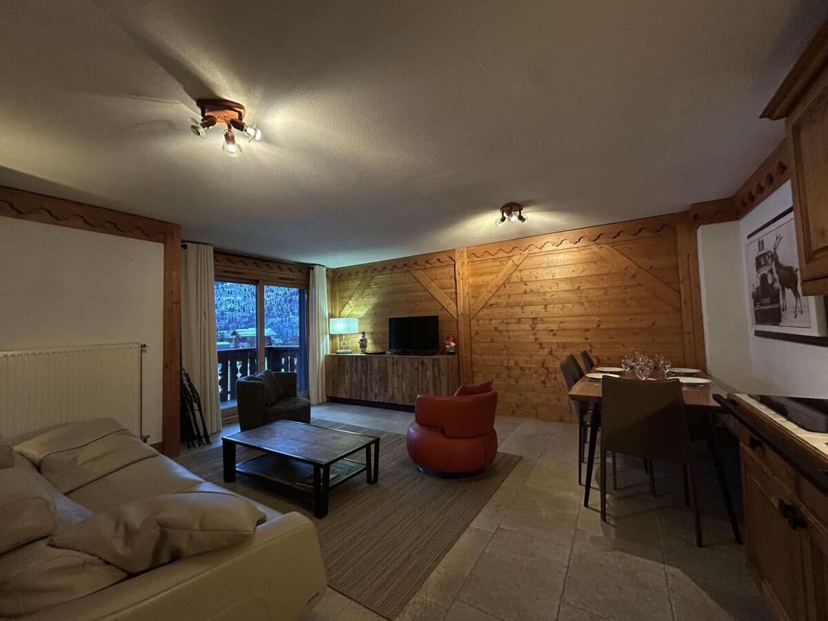 Een gezellige woonkamer met een bank, salontafel en een rode fauteuil, een eethoek met een tafel en stoelen, en een televisie op een houten wand.