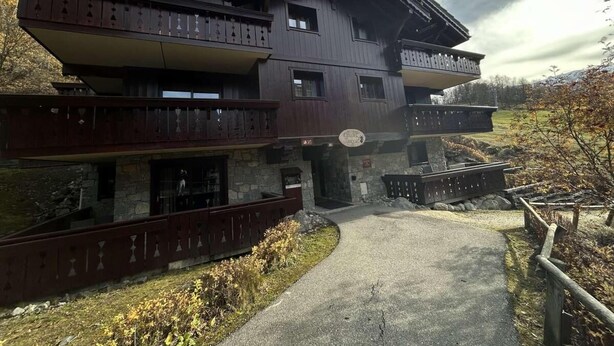 A multi-story wooden building with balconies, a stone base, and a sign indicating it is a hotel.