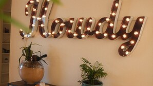 Un mur orné d’une enseigne métallique sur laquelle on peut lire le mot « Howdy », et deux plantes en pot posées sur une console.