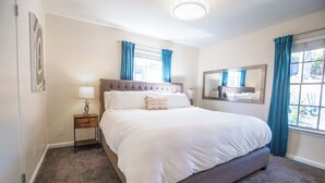 Une chambre à coucher avec un grand lit, une table de chevet, une lampe, une fenêtre avec des rideaux et un miroir sur le mur.