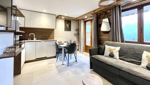 A modern kitchen with white cabinets, a dining area with a table and chairs, and a cozy living area with a sofa and cushions.