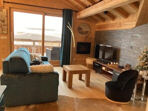 A cozy living room with a sofa, a wooden coffee table, a TV, and a fireplace.