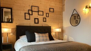 A bedroom with a bed, two bedside lamps, a wall clock, and a mirror.