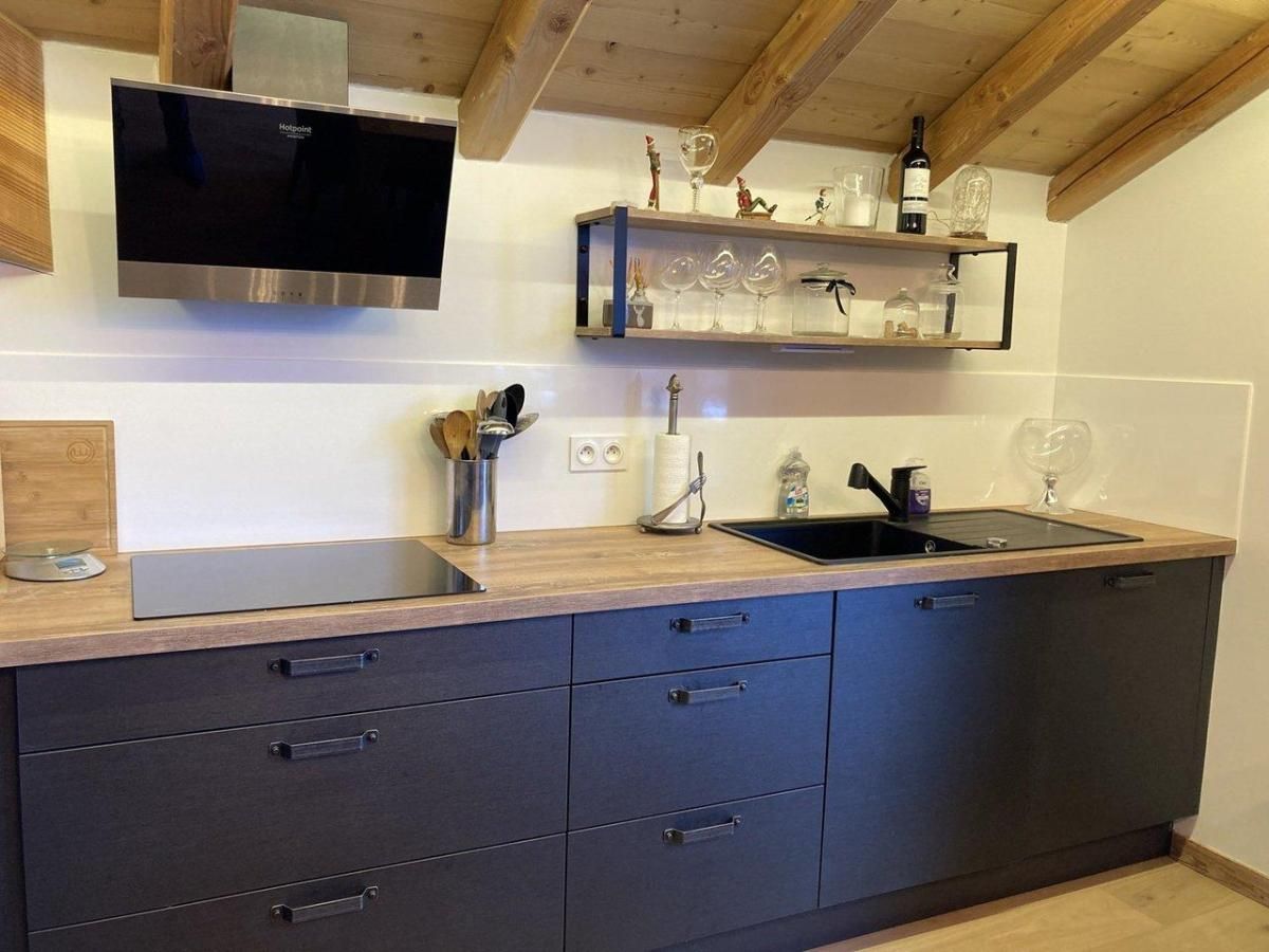 A modern kitchen with a built-in stove, a sink, and a wooden countertop. There are cabinets below the countertop and a shelf above it with glassware and decorative items.