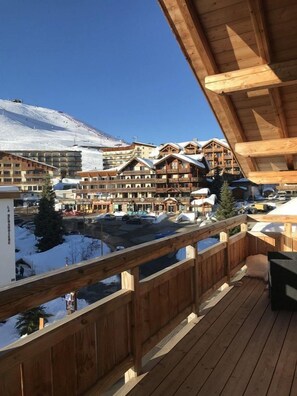 A wooden balcony overlooking a snowy mountain resort with multiple buildings and a ski slope in the background.