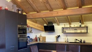 A modern kitchen with wooden beams, a dining area with a wooden table and chairs, and built-in appliances.