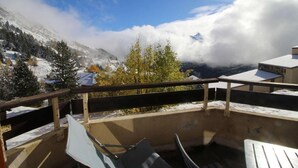 Un balcón con vista a un paisaje montañoso nevado y un edificio con techo cubierto de nieve.