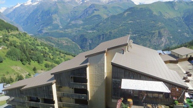 Un hotel de diseño moderno, con un edificio grande y techo inclinado y varios balcones. Se encuentra en una zona montañosa con vistas a picos nevados al fondo.