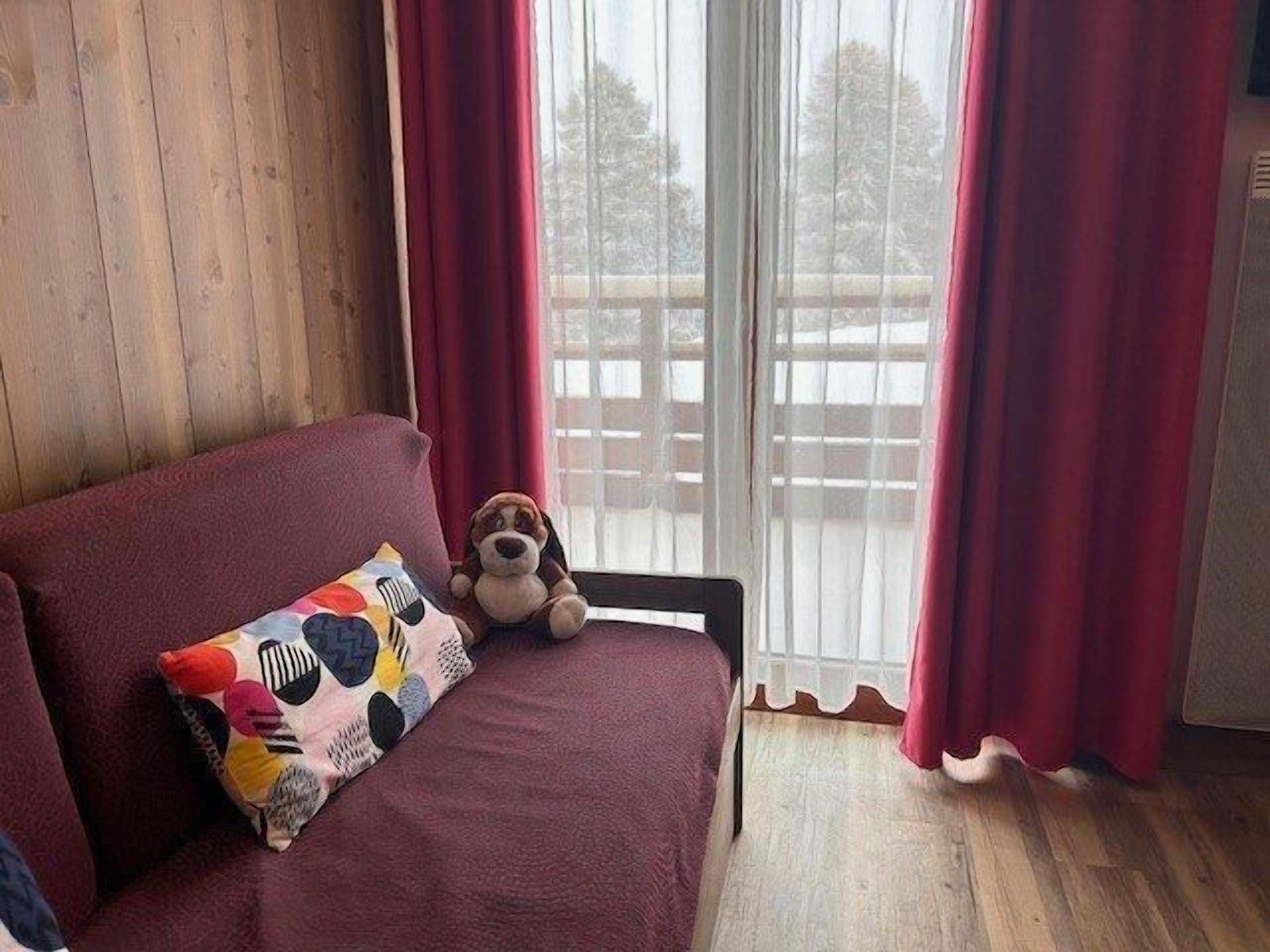 Ein gemütliches Zimmer mit Holzboden, einem roten Sofa, einem bunten Kissen und einem Stoffhund.