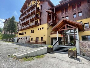 A multi-story building with balconies, a stone wall, and a gravel area.